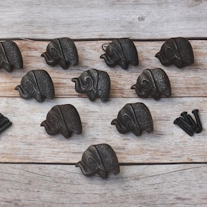 May include: Dark grey elephant-shaped cabinet knobs with detailed patterns, arranged on a light wood surface. Includes screws. These knobs are perfect for adding a unique touch to furniture.