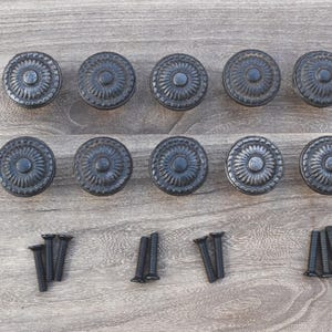 Può includere: Dieci pomelli per armadi in metallo nero con un design floreale decorativo. I pomelli sono disposti in due file da cinque. Ci sono anche tre set di viti nere.