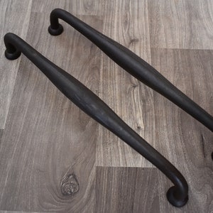May include: Two black metal cabinet pulls with a curved design. The pulls have a dark, almost black finish.