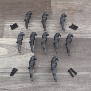 May include: Twelve black metal parrot-shaped drawer pulls with a detailed design. The pulls are arranged in three rows of four on a wooden surface.