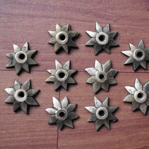 以下が含まれることがあります： 中央に穴が開いた銀色の星形をした金属製の装飾品が10個あります。これらの装飾品は、茶色の木製の表面にグリッド状に配置されています。