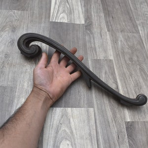 Könnte beinhalten: Eine schwarze Metallschablone mit einem dekorativen, gekräuselten Ende. Die Schablone ist etwa 30 cm lang.