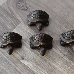 May include: Four small, dark brown cast iron turtle figurines. The turtles are arranged in a diamond shape on a wood surface.