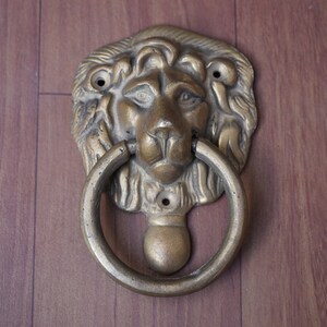 Puede incluir: Un llamador de puerta de latón con forma de cabeza de león con un anillo circular.