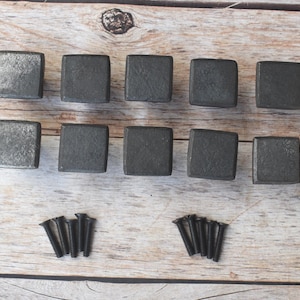 Puede incluir: Diez tiradores cuadrados de armario de color gris oscuro con una superficie texturizada están dispuestos sobre una superficie de madera clara. Dos juegos de tornillos negros están colocados debajo. Estos tiradores son adecuados para proyectos de muebles y decoración.