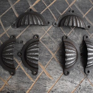 May include: Six antique-style metal cabinet door pulls with a scalloped design. The pulls are a dark grey colour and have a distressed finish.