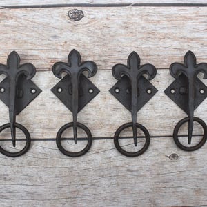 Puede incluir: Cuatro tiradores de cajón de metal negro, cada uno con un diseño de flor de lis montado sobre una placa trasera en forma de diamante con un asa de anillo circular que cuelga de la parte inferior. Los herrajes tienen un acabado mate oscuro.