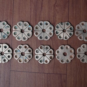 May include: Ten antique brass-colored metal discs with a flower-like design. Each disc has a central hole and eight smaller holes around the edge.