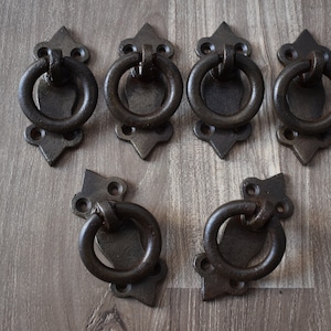 Pode incluir: Seis puxadores de gaveta de metal preto de estilo antigo com designs ornamentados e puxadores de anel.