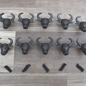 Puede incluir: Un juego de diez tiradores negros para armarios con forma de cabeza de toro y tornillos a juego. Los tiradores, de hierro fundido, presentan cuernos y rasgos faciales detallados. Ideal para añadir un toque rústico o western a los muebles.