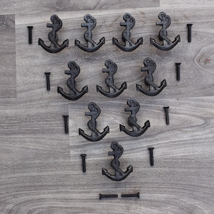 Könnte beinhalten: Zehn schwarze Anker-Schubladengriffe aus Metall mit Schrauben. Die Anker sind mit einem Seil verziert und haben eine rustikale Oberfläche.