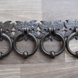 May include: Four antique-style black metal door knockers with ornate floral designs. Each knocker has a circular ring and a rounded knob.