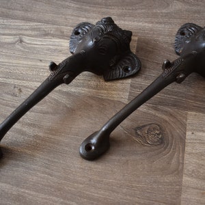 Op de afbeelding: Twee zwarte metalen deurgrepen met een olifantenkopontwerp. De grepen zijn gebogen en hebben een decoratief ontwerp.
