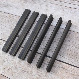 May include: Six dark brown, rectangular cabinet pulls arranged in a parallel row. Each handle features a smooth, elongated design with a slightly curved top surface and flat sides, providing a consistent look for furniture or cabinetry hardware.