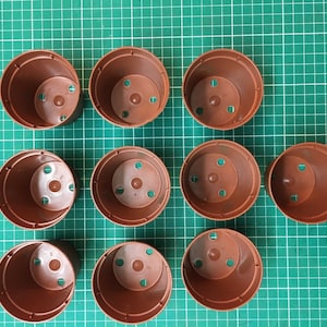 Pode incluir: Dez vasos de plantas de plástico castanho com orifícios de drenagem. Os vasos estão dispostos em três filas numa superfície de grelha verde.
