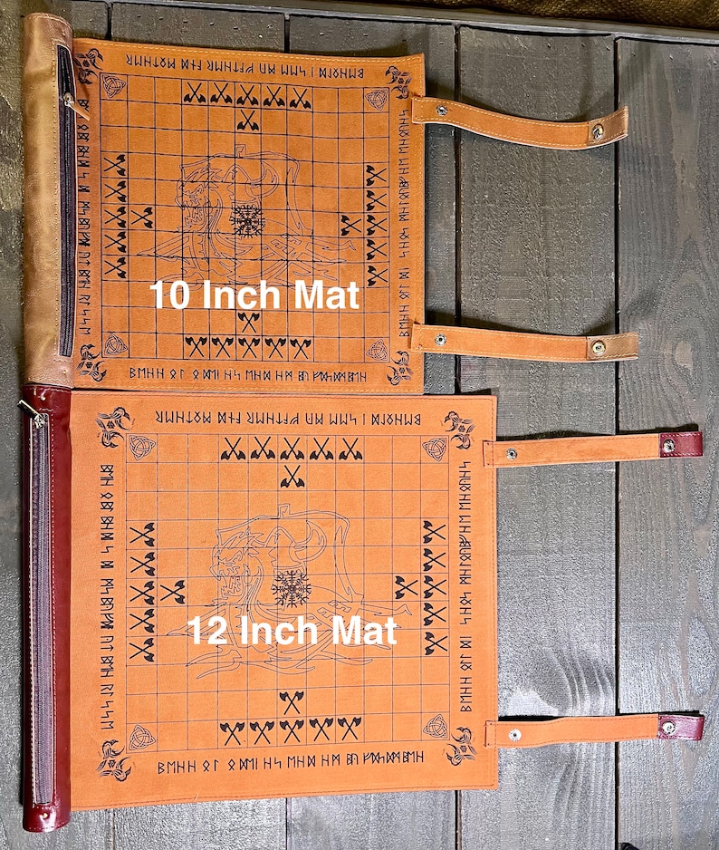 以下が含まれることがあります： 「10 Inch Mat」と「12 Inch Mat」と書かれた2つのタン革製ゲームマット。各マットは、バイキングをテーマにしたイラストとテキストが施されたグリッドデザインが特徴です。マットには固定用のストラップとジッパー付きのエッジが付いています。