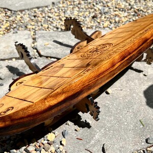 Puede incluir: Una mesa de centro de madera con forma de tabla de surf y acabado marr&oacute;n claro. La mesa tiene un dise&ntilde;o detallado tallado en la superficie y est&aacute; sostenida por patas de madera decorativas. La mesa mide aproximadamente 152 cm de largo.