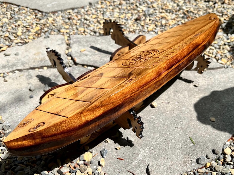 Puede incluir: Una mesa de centro de madera con forma de tabla de surf y acabado marr&oacute;n claro. La mesa tiene un dise&ntilde;o detallado tallado en la superficie y est&aacute; sostenida por patas de madera decorativas. La mesa mide aproximadamente 152 cm de largo.
