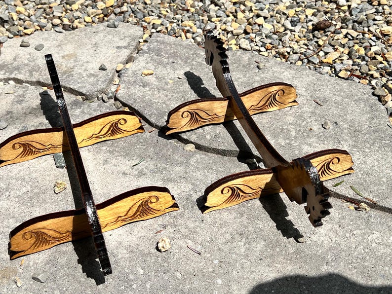 Puede incluir: Expositores de madera con dise&ntilde;o de olas. Los expositores est&aacute;n hechos de madera de color claro con un borde y un patr&oacute;n de olas marr&oacute;n oscuro. Los expositores est&aacute;n dise&ntilde;ados para sostener objetos y se exhiben al aire libre.