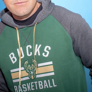 Może przedstawiać: Zielono-szara bluza z kapturem z napisem "Bucks Basketball" i logo jelenia z przodu.