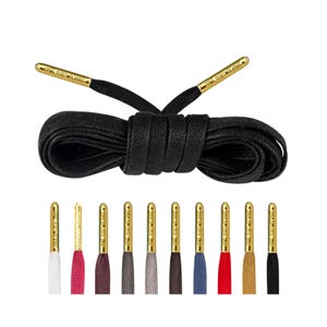 May include: Black shoelaces with gold aglets. The shoelaces are made of a flat, woven material. The aglets are engraved with the words "Gold Standard".