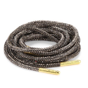 May include: A pair of black shoelaces with gold tips, covered in sparkling rhinestones.