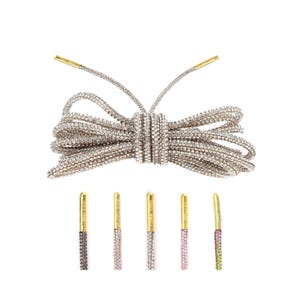 May include: A pair of shoelaces with a gold tip and a silver body covered in rhinestones. The shoelaces are tied in a bow. There are five additional shoelaces in different colors, each with a gold tip and a silver body covered in rhinestones.
