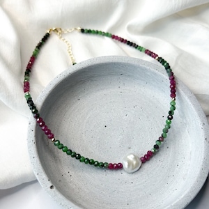 May include: A delicate necklace made with green and pink gemstone beads and a single white pearl pendant.