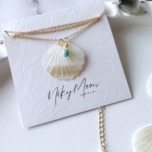 May include: Gold chain necklace with a white seashell pendant and a small turquoise gemstone. The necklace is displayed on a white card with the text "Nicky Moon Jewelry".