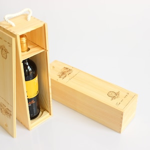 May include: A wooden wine bottle gift box with a bottle inside. The box is open, revealing the bottle with a yellow label. A second closed box is next to it. Both boxes have decorative etchings and a rope handle.