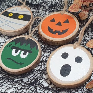 May include: Four wooden ornaments with Halloween themes. A mummy, a pumpkin, a Frankenstein, and a ghost. Each ornament is painted with a different character and has a string for hanging.