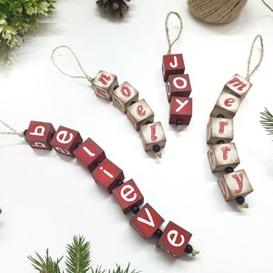May include: Four red wooden ornaments with white lettering spelling out "believe", "joy", "merry", and "home". Each ornament is strung together with twine and black beads.
