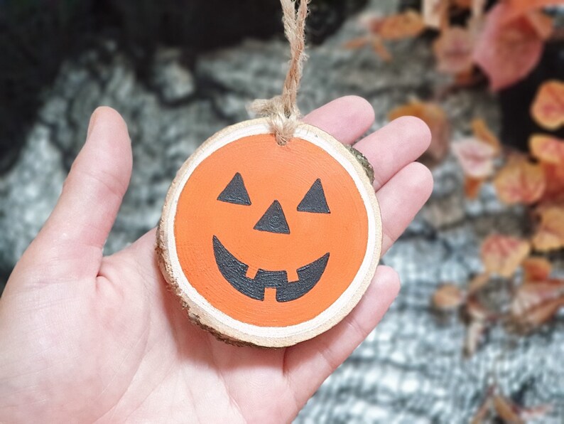 May include: A wooden pumpkin ornament with a painted orange face and black eyes, nose, and mouth. The ornament has a string attached for hanging.