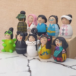 May include: A collection of 10 hand-painted wooden dolls with various colorful designs and patterns. The dolls are dressed in different outfits, including a plaid shirt, a white shirt with a black design, a blue shirt with a star pattern, a pink shirt with a white design, a green shirt with a white design, a black dress, a white dress with a black design, a yellow dress with a floral design, a black and white dress with a red design, and a green and white dress with a black design.