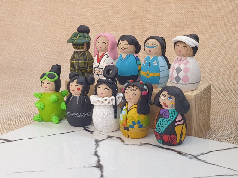 May include: A collection of 10 hand-painted wooden dolls with various colorful designs and patterns. The dolls are dressed in different outfits, including a plaid shirt, a white shirt with a black design, a blue shirt with a star pattern, a pink shirt with a white design, a green shirt with a white design, a black dress, a white dress with a black design, a yellow dress with a floral design, a black and white dress with a red design, and a green and white dress with a black design.