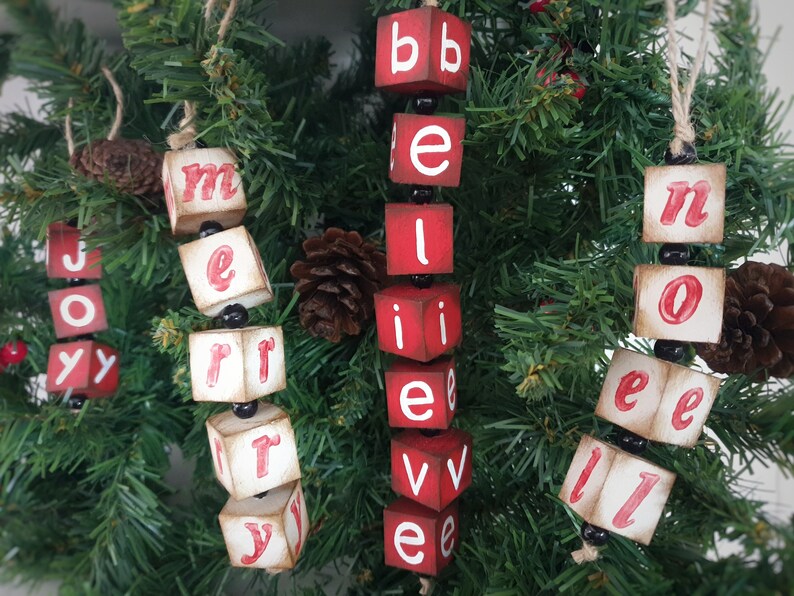 May include: Four wooden Christmas decorations spelling out "Merry", "Believe", "Noel", and "Joy" with red letters and black beads.