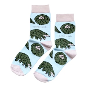 May include: A pair of light blue socks with a repeating pattern of green pangolins and curled-up pangolins. The socks have light pink cuffs, heels, and toes. The text "BARE KIND" is printed on each sock.