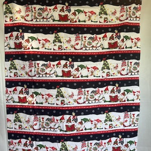 May include: A rectangular fabric panel featuring a repeating horizontal pattern of Christmas gnomes on a white background, separated by black bands with white snowflakes. The gnomes wear red and green hats and are depicted with trees and gifts.