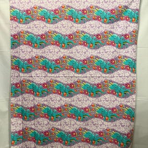 May include: A fabric with a repeating pattern of teal dinosaurs and pink flowers on a lavender background. The design includes white floral accents. The word "ROAR!" is visible at the bottom of the fabric.