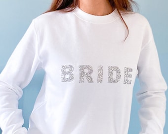 May include: White sweatshirt with the word "BRIDE" spelled out in silver glitter.