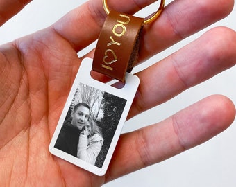 Op de afbeelding: Een witte foto sleutelhanger met een zwart-wit foto van een stel. De sleutelhanger heeft een bruin leren bandje met de tekst "I ♥ You" in gouden letters.