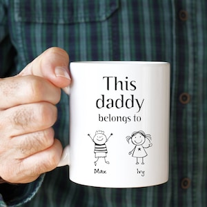 Puede incluir: Taza de cerámica blanca con texto negro que dice "Este papá pertenece a" con dibujos de figuras de palo de un niño y una niña con los nombres Max e Ivy debajo.