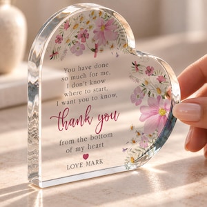 May include: A heart-shaped clear acrylic plaque featuring a floral design with pink and white flowers. The text reads: You have done so much for me, I don't know where to start, I want you to know, thank you from the bottom of my heart. LOVE MARK.