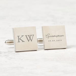 Può includere: Un paio di gemelli quadrati argentati. Un gemello presenta le iniziali "KW", mentre l'altro riporta la scritta "Groomsman" e la data "29.09.2025". I gemelli hanno una finitura lucida e una chiusura a T.