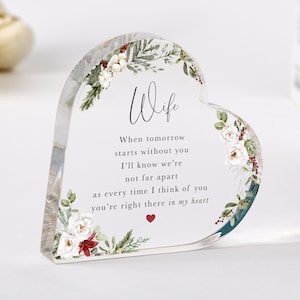 Op de afbeelding: Een hartvormig aandenken van helder acryl met het woord "Wife" en een liefdevolle boodschap. De randen zijn versierd met witte bloemen, groene bladeren en rode accenten. Een klein rood hart staat onderaan de boodschap.