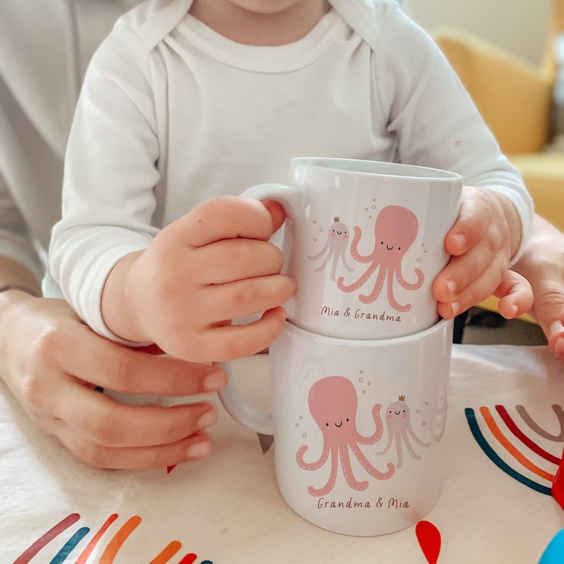 May include: Two white ceramic mugs with pink octopus illustrations. The top mug says "Mia & Grandma" and the bottom mug says "Grandma & Mia".