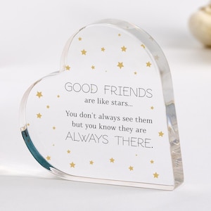 Può includere: Un oggetto decorativo trasparente a forma di cuore con il testo "GOOD FRIENDS are like stars... You don't always see them but you know they are ALWAYS THERE." Stelle dorate adornano lo sfondo bianco.