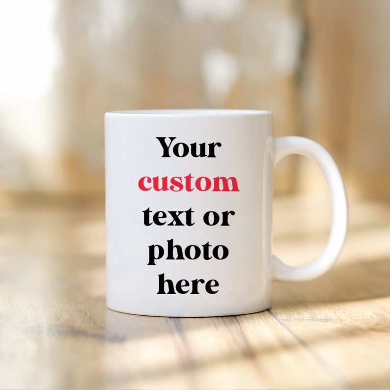 May include: White ceramic coffee mug with black text that reads "Your custom text or photo here". The word "custom" is in red.