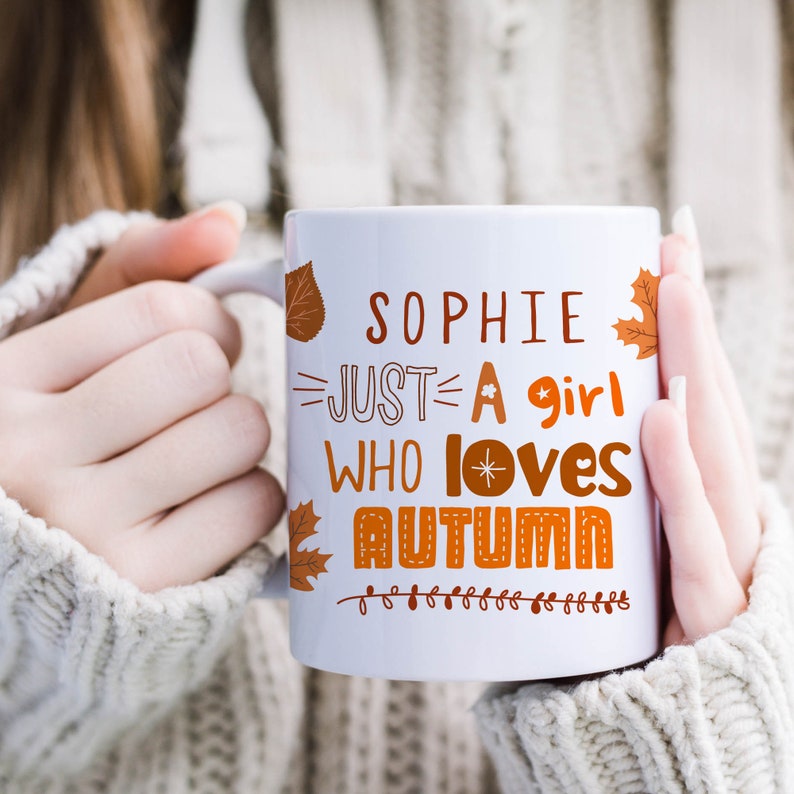 May include: White ceramic mug with a brown and orange design. The mug says "Sophie Just A Girl Who Loves Autumn" with a star and heart design.