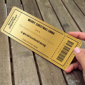 May include: A gold-coloured ticket with the text "This is your GOLDEN TICKET" and "MERRY CHRISTMAS EMMA". The ticket says "This ticket entitles you and me to a special weekend away" and is signed "Lots of love Jack". The ticket also has a barcode and the text "KRMSBTO 2022".